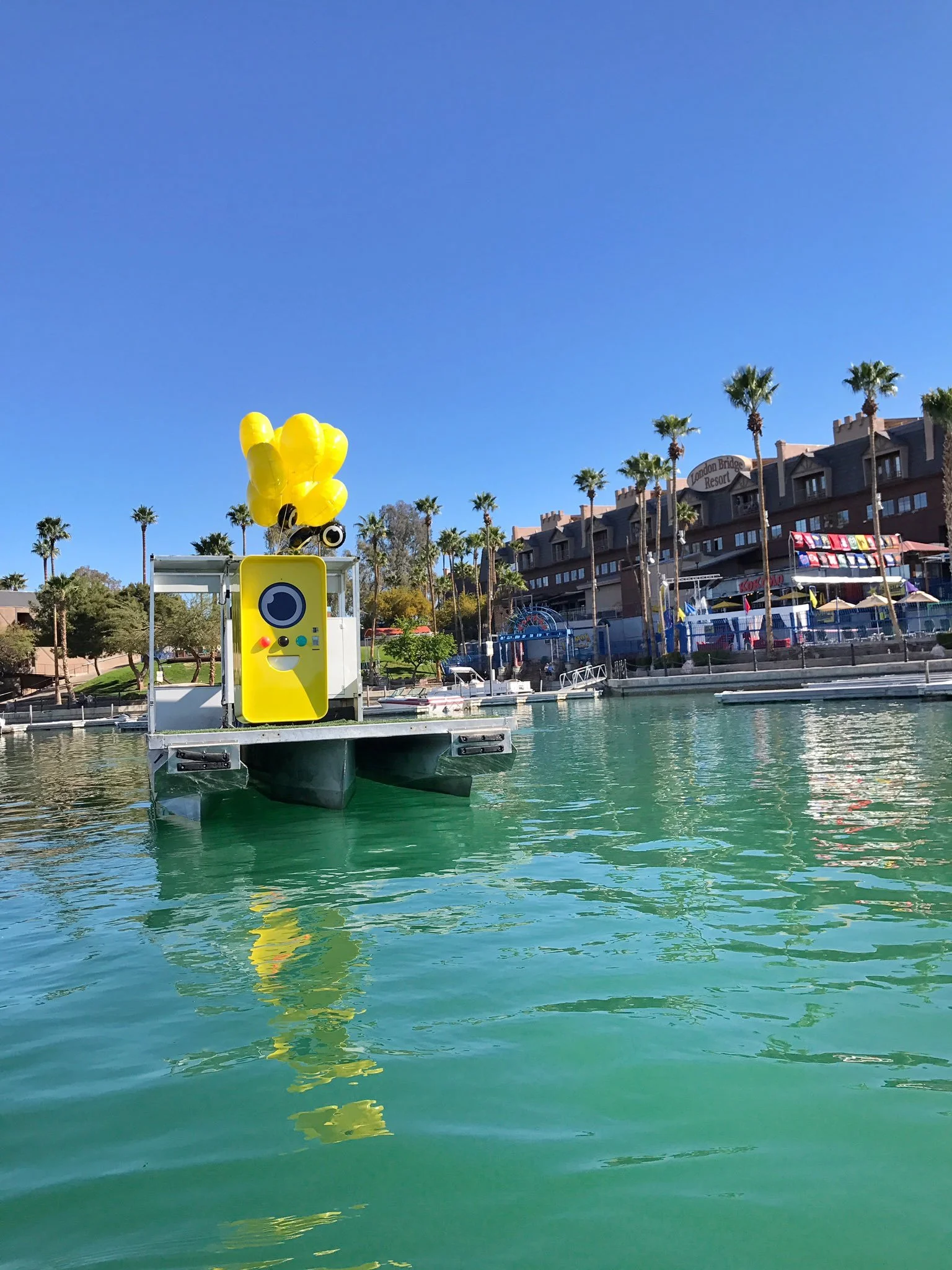 Yellow Snapbot vending machine on a floating pontoon barge with yellow balloons, moored across from London Bridge Resort